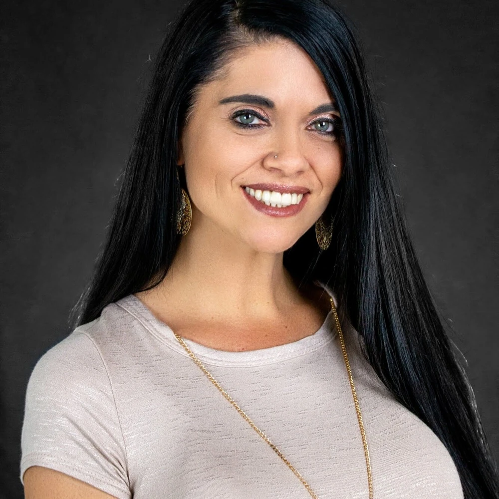 Portrait of Dana Caylor - Long black hair and white shirt on a dark background.